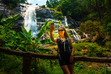 Young Woman Wearing Sunglasses Takes Selfie On Her Smartphone With Wachirathan Waterfall In The Background Doi Inthanon National Park