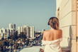 © flowertiare - woman in a pink shirt standing on the balcony and listening music in a headphones against the city background