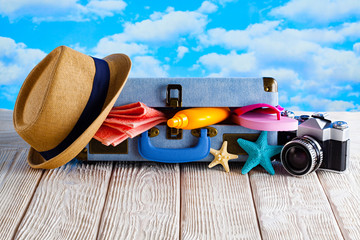 Wall Mural - Open holiday suitcase; summer hat, towel, tanning oil, photo camera; flip flops on wooden table