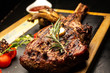 Grilled Tomahawk steak ribeye with rosemary, butter and cherry tomatoes on wooden plate