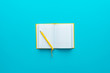 © Ruslan Grumble - Top view of opened notebook and yellow pen over it in the centre of turquoise blue background with copy space. Minimalist flat lay image of blank diary and ball-point pen