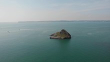 An Aerial Backward Footage Of A Rocky Island Rock (Thatcher Point) With Speeding Boat And Kayakers Along Rocky Cliff And Turquoise Water Under A Majestic Blue Sky