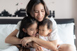 © Kawee - Happy Asian family activity concept. Beautiful mother hugging her children with smile sitting on bed in bedroom. Older sister feeling funny and teasing the baby with happiness. Lovely expression.