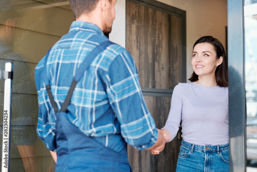 Happy young client of maintenance service shaking hand of technician
