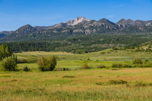 The Rocky Mountains Rise Above A Landscape Of Green Grassy Fields And Meadows On A Ranch Near Pagosa Springs, Colorado