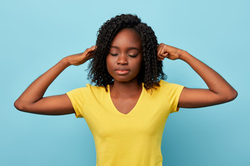 serious beautiful American girl with closed eyes closing her ears with palms, isolated blue background. studio shot. concentration concept