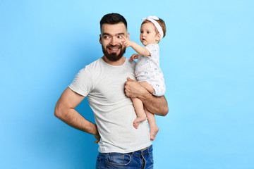 little girl showing something to her dad while sitting in his arms. close up photo. isolated blue background. cute clever baby pointing at somewhere.