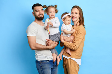 happy young couple and their kids posing to the camera. love, friendship concept. isolated blue background