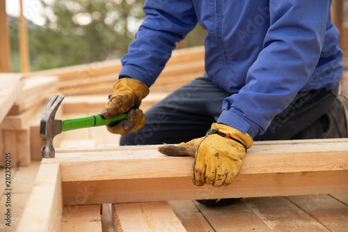 Male builder in yellow gloves hammer nail into wooden structure Poster Mural XXL
