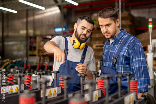 Cuadros en Lienzo Young trainee looking at industrial equipment while listening to manager