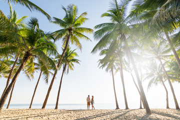 couple standing on sandy beach among palm trees on sunny morning