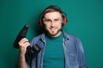 Young working man with power drill on green background