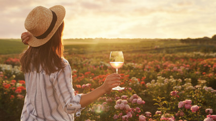 Poster - Woman with glass of wine in rose garden on sunny day. Space for text