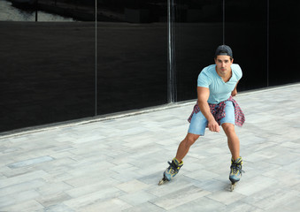 Poster - Handsome young man roller skating near glass building on city street, space for text