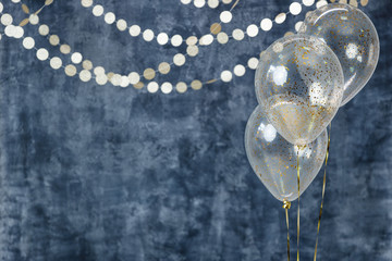 Three balloons with confetti and gold garlands on a smoky dark blue background. Birthday and holiday decor.