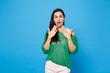 © ViDi Studio - Portrait of shocked amazed young woman in green casual clothes keeping mouth open, covering mouth with hands isolated on bright blue background in studio. People lifestyle concept. Mock up copy space.