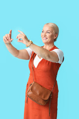 Poster - Stylish mature woman showing something on color background