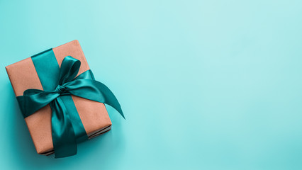 gift box in craft wrapping paper and green satin ribbon on turquoise blue background, copy space rig