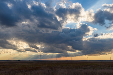 sandy beach in the light of the setting sun with a huge cloud in the sky, wind generators standing in the field.