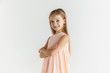© master1305 - Stylish little smiling girl posing in dress isolated on white studio background. Caucasian blonde female model. Human emotions, facial expression, childhood. Standing with hands crossed.