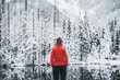 One girl hiker stands in front of a winter lake looking to the snowy landscape. Rear view.