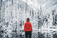 One Girl Hiker Stands In Front Of A Winter Lake Looking To The Snowy Landscape. Rear View.