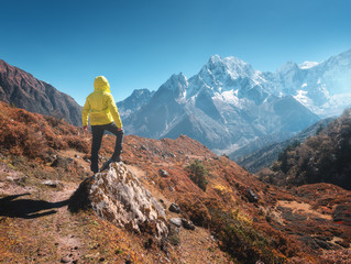 Wall Mural - sporty man on the stone is looking on snow covered mountains at sunny day. landscape with guy in yel
