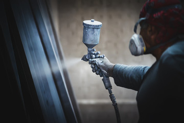 Man painting metal products with a spray gun