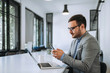 © bnenin - Confident businessman using phone indoors.