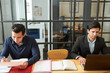 © DragonImages - Two young businessmen sitting at the table doing paperwork and working on laptop computer at modern office