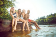 © master1305 - Group of happy friends having fun while sitting and laughting on the pier on river. Joyful women and men in swimsuit at riverside in sunny day. Summertime, friendship, resort, relations concept.
