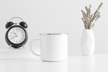 Enamel mug mockup with a lavender in a vase, book and a clock on a white table.