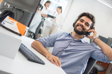 Wall Mural - Cheerful friendly smiling customer support agent with headset assisting client in while working in call centre