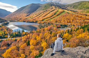 Woman hiking at Artist's Bluff in autumn. View of Echo Lake. Fall colours in Franconia Notch State Park. White Mountain National Forest, New Hampshire, USA