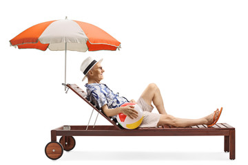 Wall Mural - Elderly man enjoying on a sunbed under umbrella with an inflatable beach ball