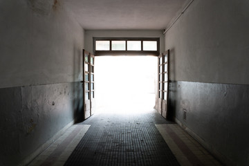 Wall Mural - empty gloomy square arch of an old house with light on exit.