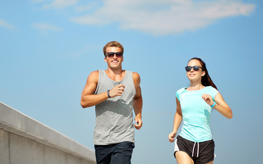 Poster - fitness, sport and lifestyle concept - happy couple in sports clothes and sunglasses running outdoors