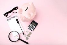 Pink Piggy Bank With Notebook, Coins And Magnifying Glass On Pink Background