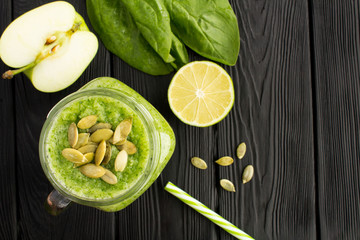 Wall Mural - Green smoothies with spinach, apple and pumpkin seeds  on the black wooden background.Top view. Copy space.