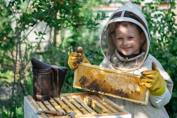 Wall Mural - Cheerful boy beekeeper in protective suit near beehive. Honeycomb with honey. Organic food concept. The most useful organic honey.