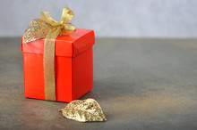 Red Gift Box With A Gold Ribbon. The Gift Is Decorated With Gold Leaves. Free Space For Text. Close-up.