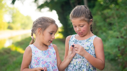 Authentic shot of two happy little girls sisters are eating a fresh biologic blackberries just harvested by themselves in a forest.