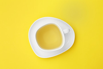 Cup of tea and saucer on yellow background, top view