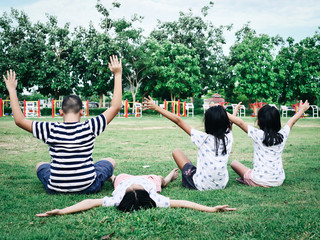 Back of boy and girl sitting on green grass in the park outdoor.