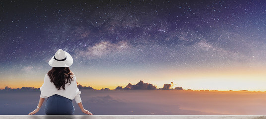 Wall Mural - Young woman in white hat looking at horizon with sky full of stars at dawn	