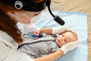 From above doctor with special tool on head checking eyes of adorable baby lying on bed