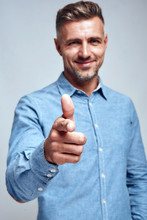 I Am Choosing You. Smiling Handsome Man In Blue Shirt Pointing His Finger And Smiling At Camera While Standing Against Grey Background