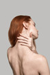 Elegant beauty. Back view of young and beautiful redhead woman touching her neck while standing against grey background