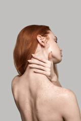 elegant beauty. back view of young and beautiful redhead woman touching her neck while standing agai