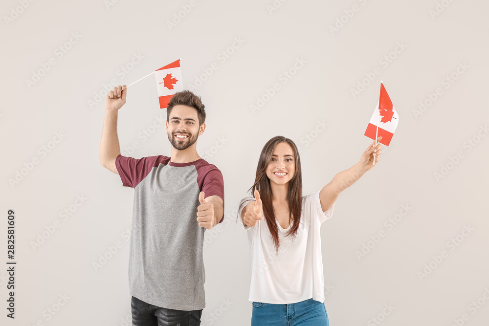 Young people with Canadian flags on light background